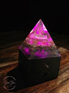 SoulStone Designs orgonite pyramid lamp with pink light, featuring copper, crystals, and a wooden base. Supports focus and calm.