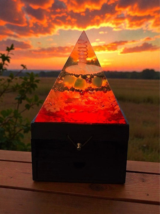 Soul Stone Designs Solar Current orgonite pyramid with Citrine, Pyrite, Green Aventurine, Sunstone, Clear Quartz, Selenite, and copper coil on a wooden box, illuminated by multicoloured LEDs.