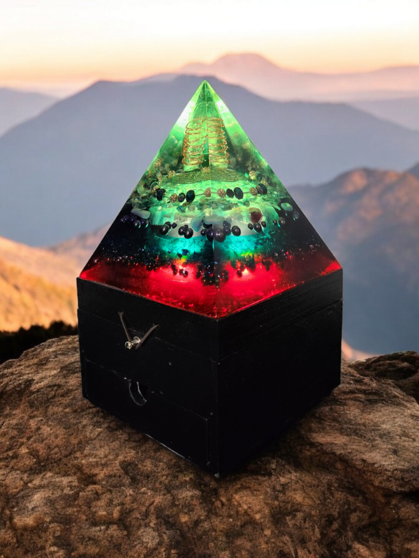 Handcrafted orgonite pyramid energy generator glowing with green and red light on a mountain at sunrise