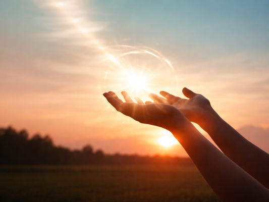 Outstretched hands holding radiant light at sunset, representing coherence and living in balance and flow. 
