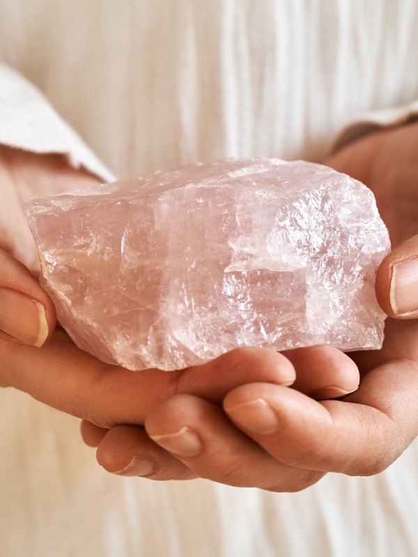 Hand holding a raw rose quartz crystal for calm, clarity and focused energy.