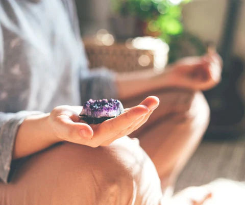 Person meditating while holding an amethyst crystal in their palm, promoting calm, focus, and spiritual grounding.