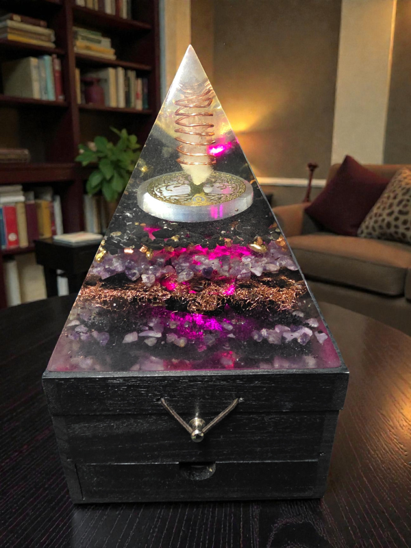 Pyramid-shaped decorative object with glowing pink and purple interior on a table.