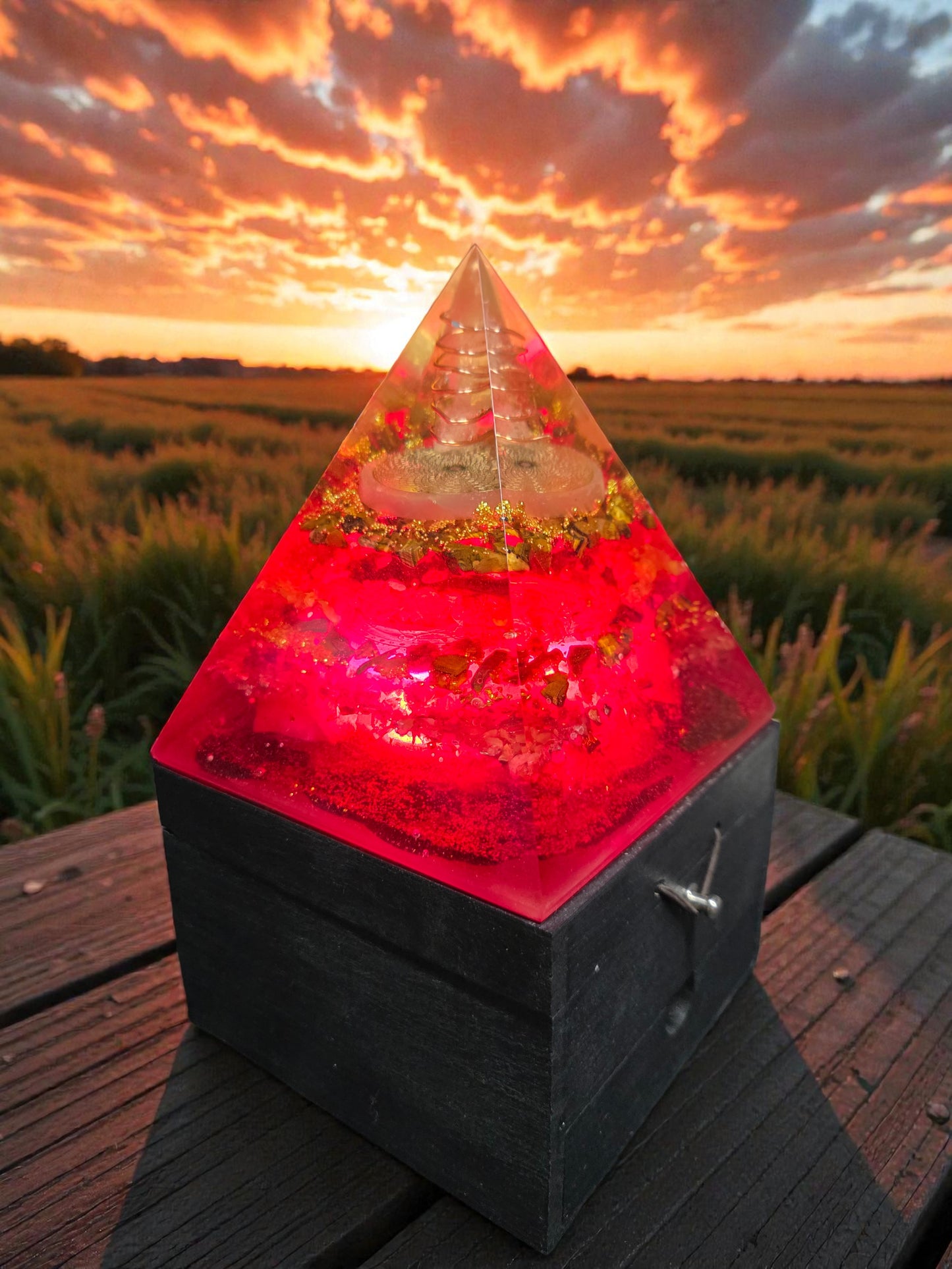 Pyramid-shaped light with red glow on a wooden surface against a sunset sky