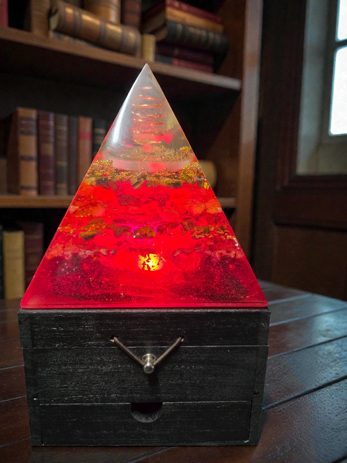 Pyramid-shaped lamp with a red base and clear top on a wooden surface.