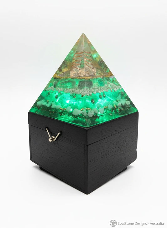SoulStone Designs Celestial Clarity orgonite lamp with green crystals and copper spiral detail. Pyramid shape on a black wooden base.