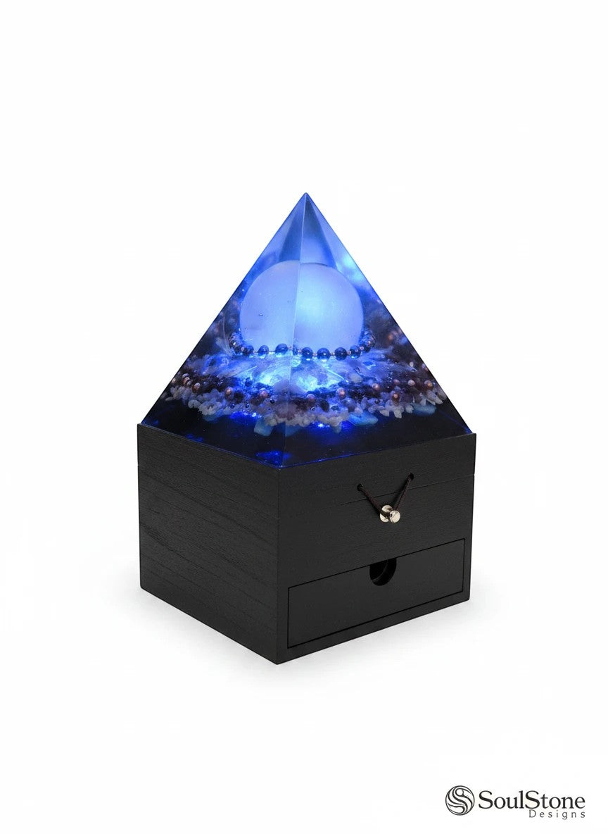 SoulStone Designs orgonite pyramid lamp with blue light, selenite sphere, and embedded crystals. Black wooden base with drawer.