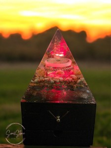 SoulStone Designs orgonite pyramid lamp with copper and crystals, emitting a soft pink glow, set on a wooden base.