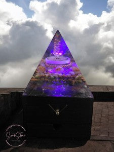 SoulStone Designs orgonite pyramid lamp with purple light, crystals, copper, and wooden base. Supports focus and calm.