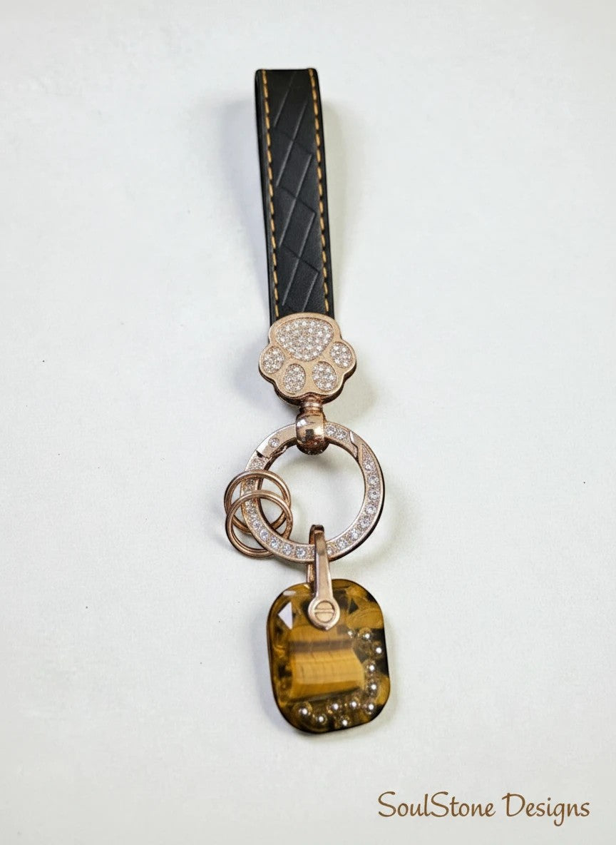 SoulStone Designs keychain with black leather strap, rose gold paw charm with crystals, and a tiger's eye stone pendant.