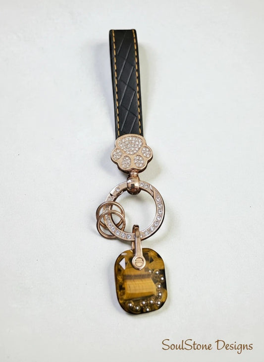 SoulStone Designs keychain with black leather strap, rose gold paw charm with crystals, and a tiger's eye stone pendant.