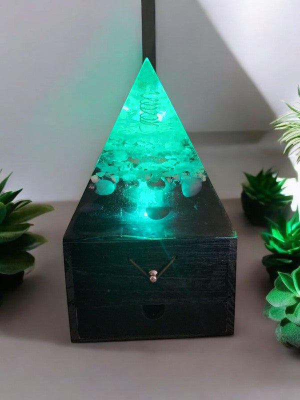 Soul Stone Designs Celestial Drift Orgonite Lamp with green light, crystals, and copper coil in a pyramid shape atop a wooden box.