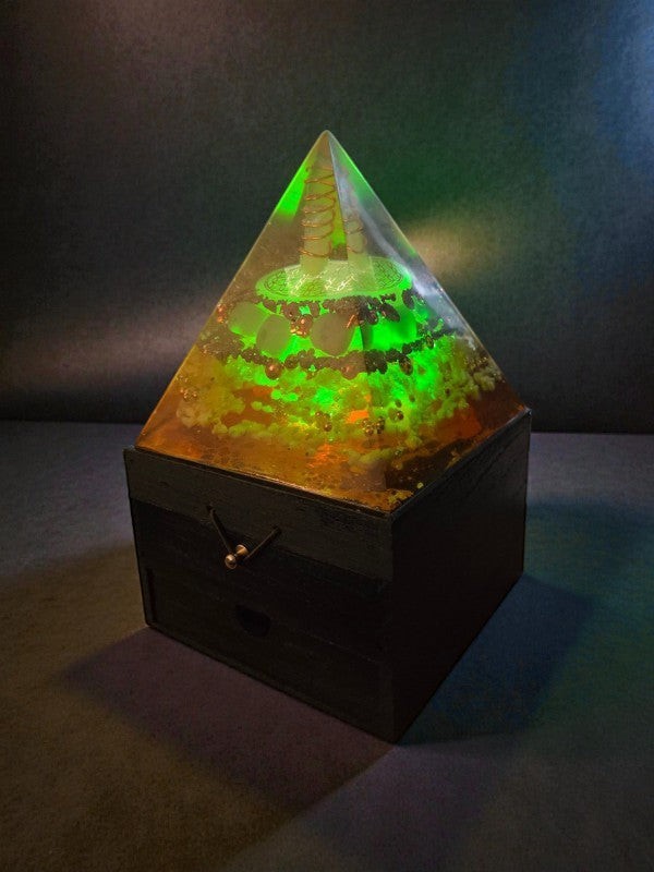 Soul Stone Designs Solar Current orgonite pyramid with Citrine, Pyrite, Green Aventurine, Sunstone, Clear Quartz, Selenite, and copper coil on wooden box, illuminated by multicolor LED.