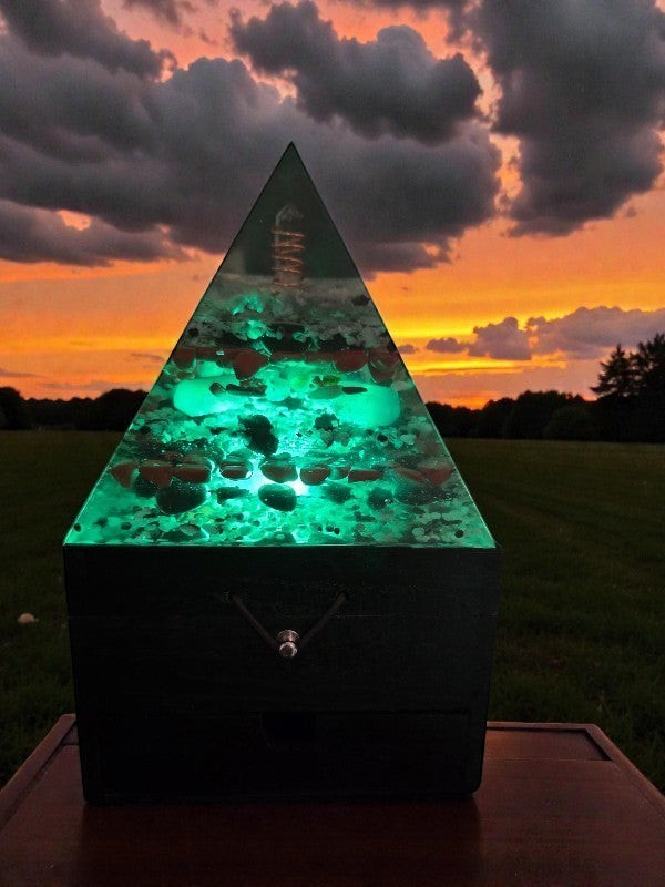 Soul Stone Designs Aegis Root orgonite pyramid lamp with green glow, clear quartz point, copper coil, and embedded stones.
