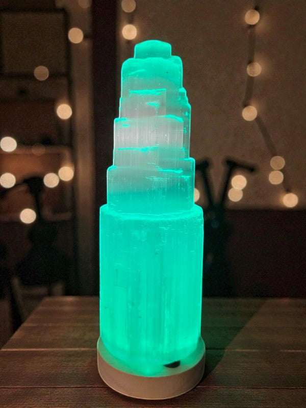 Soul Stone Designs tall white Selenite tower with teal light, natural striations, on a wooden table.